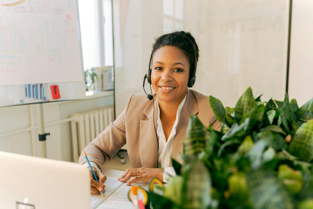 Friendly call center agent smiling at her desk with headset in a bright office environment.